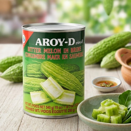 Aroy-D bitter melon can on a table with green vegetables and a blurred background